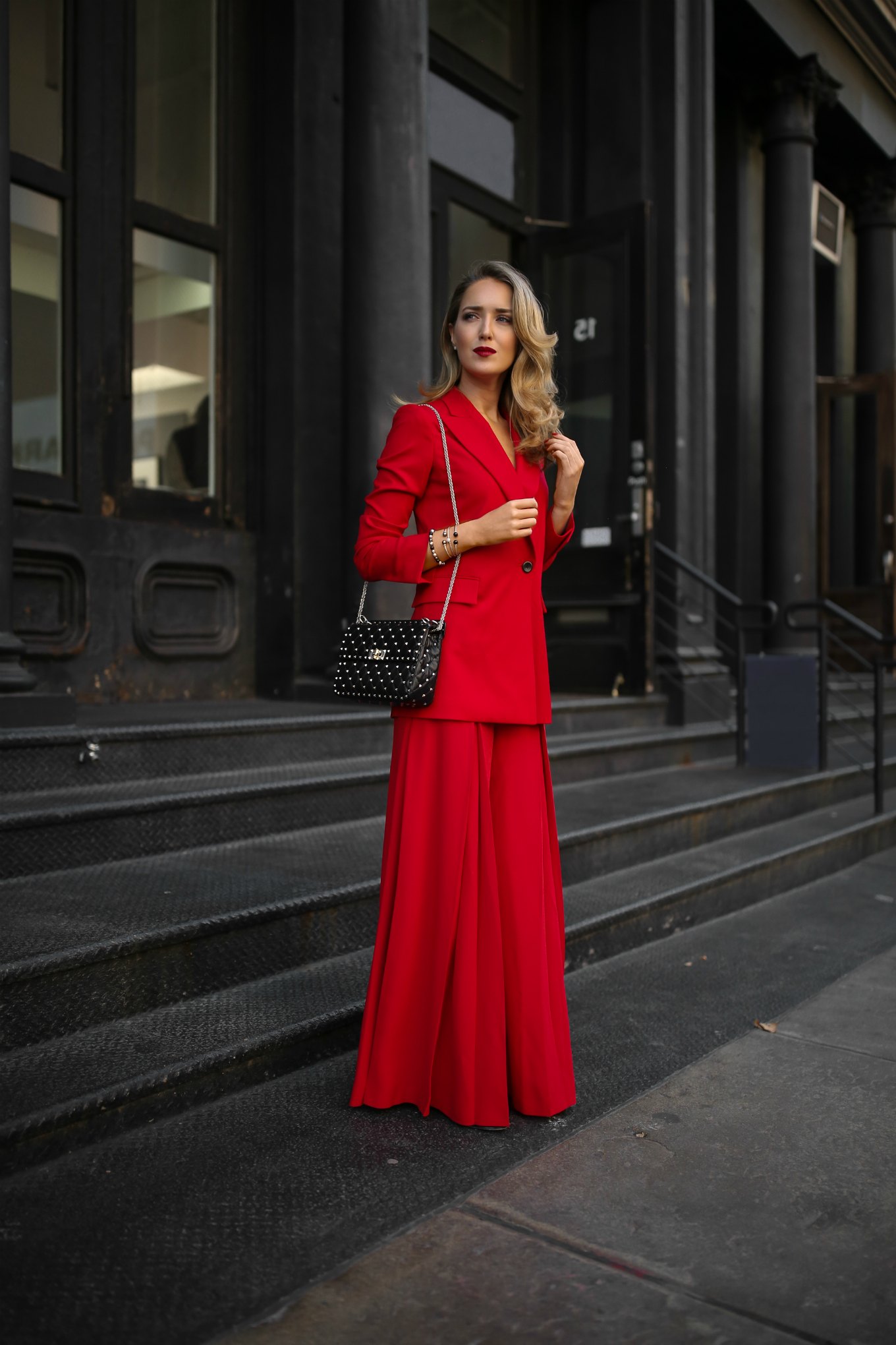 Mary Orton of Memorandum wears a Sara Battaglia red longline blazer, wide-leg pleated red trousers, a black Valentino studded leather shoulder bag, stacked David Yurman Solari bracelets and David Yurman pave stud earrings