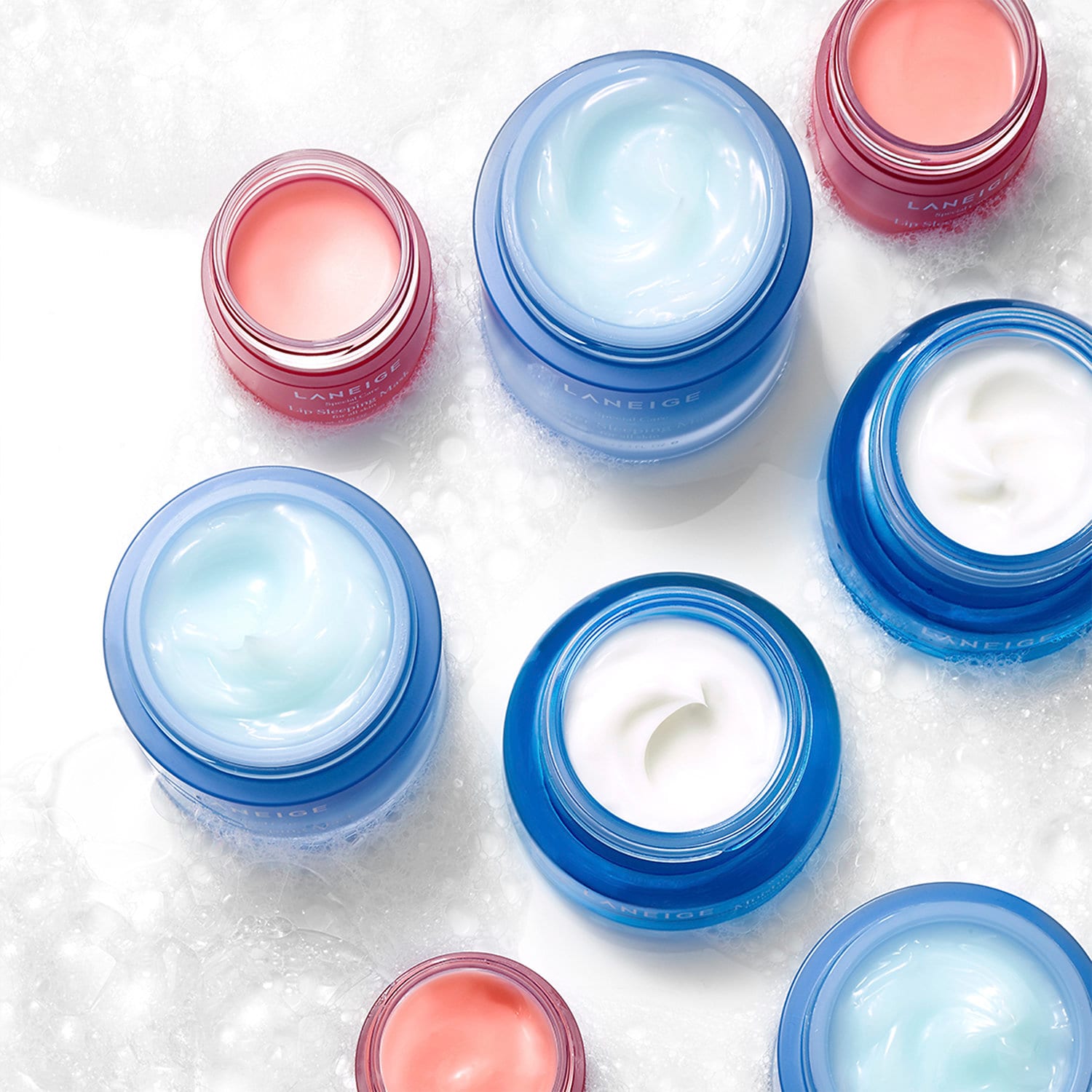 laneige products Several open blue and pink jars of Laneige beauty products including lip sleeping mask on white sudsy background